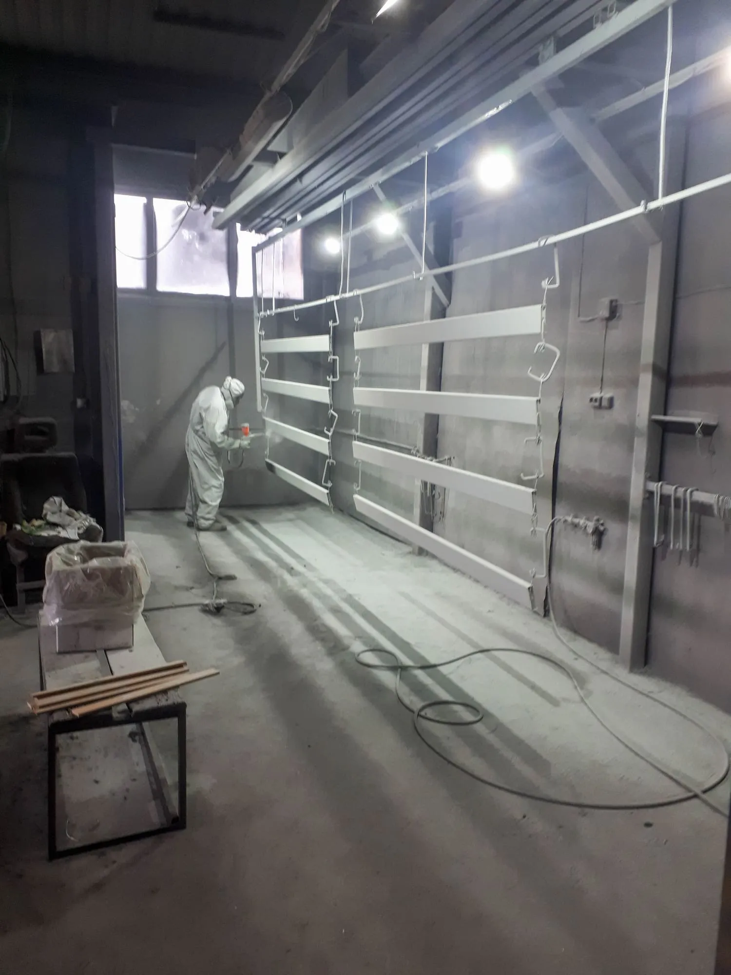 Technician in full protective suit spray-applying coating to structural steel beams inside a controlled shop booth