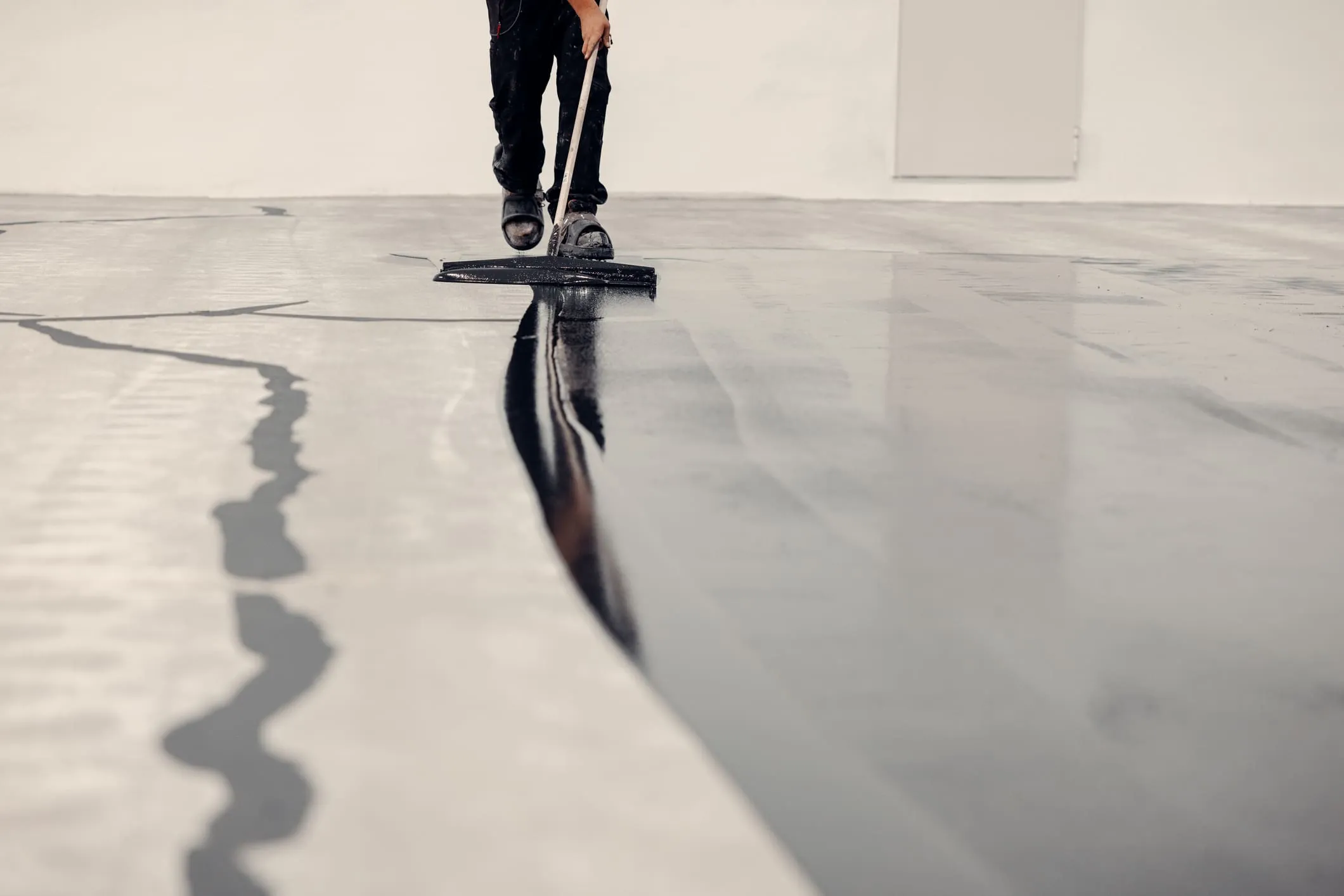 Applicator spreading a self-leveling epoxy floor coating with a squeegee across a large industrial floor