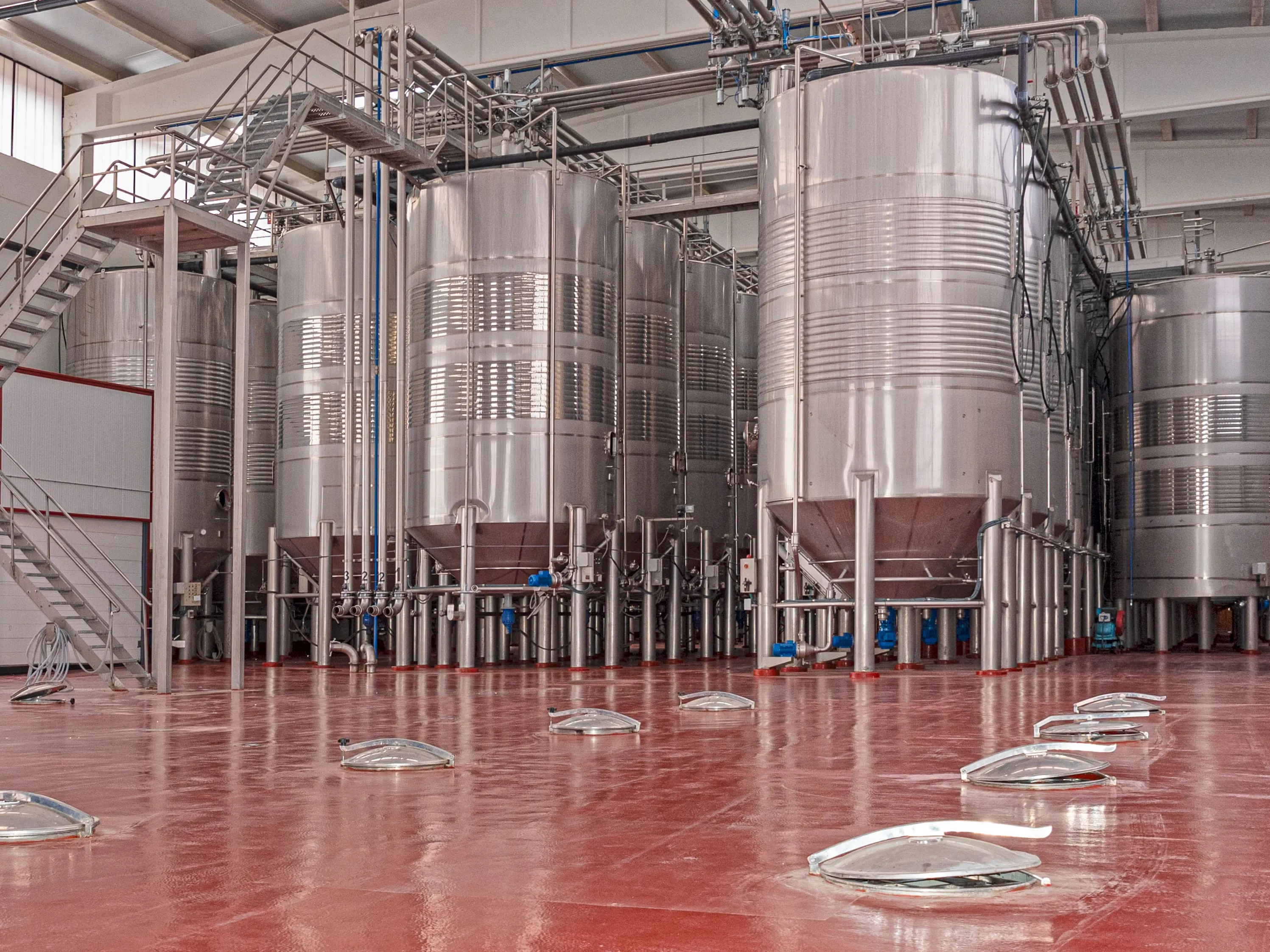 Row of polished stainless steel storage tanks inside a processing facility with a glossy red epoxy-coated floor